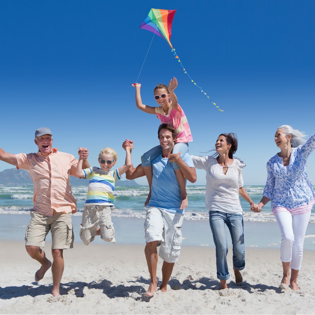 Family of 4 and grandparents flying kite at the beach